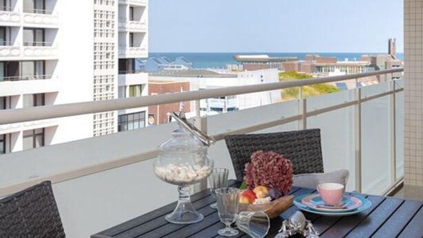 Un balcón con una mesa preparada para dos personas, con vistas a la ciudad y al mar.