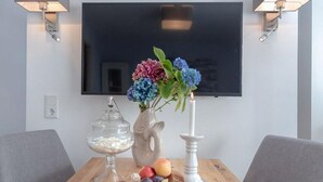 Una habitación moderna con un televisor de pantalla plana en la pared, una mesa de madera con frutero, jarrones decorativos y una vela.