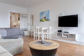 Ein modernes Wohnzimmer mit einer Couch, einem runden Couchtisch, einem Fernseher und einem Gemälde eines Leuchtturms.