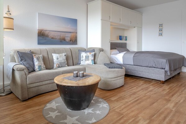 Ein modernes Wohnzimmer mit einer Couch, einem runden Couchtisch, einem Bett und einem Bild an der Wand.
