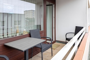 Ein Balkon mit einem Holztisch, zwei Stühlen, einer Glastür und Blick auf Gebäude.