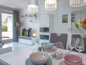 A modern dining area with a white table set for two, a television, and a view of the outdoors. - SYLTROSE - Syltrose - Spacious 2-room apartment in a central yet quiet location with (Sylt)