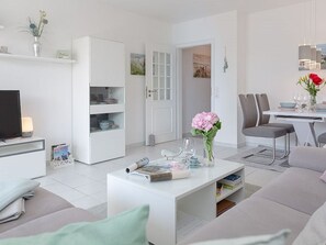 Una sala de estar moderna con un sofá blanco, una mesa de centro con revistas, un televisor y un comedor con sillas y una mesa.