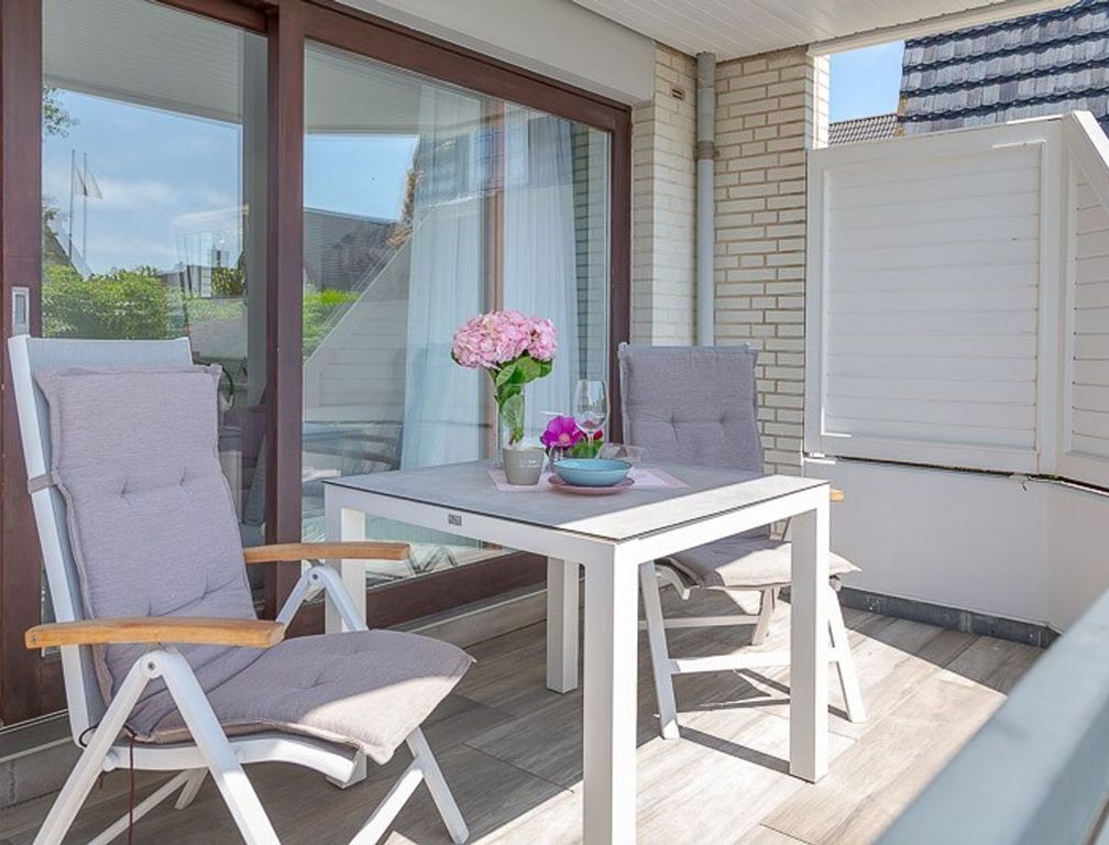 Een buitenzitplaats met twee stoelen en een tafel, een potplant en een uitzicht door een glazen deur.