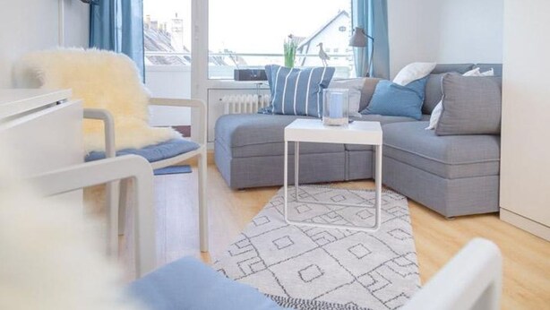Ett modernt vardagsrum med en grå soffa, en vit fåtölj och en mönstrad matta.