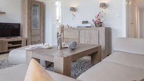 A modern living room with a sofa, a wooden coffee table, a TV, and a cabinet. - Beachwalk - Brandenburg House: 3-room apartment, 2 bedrooms, balcony, ideal for (Sylt)