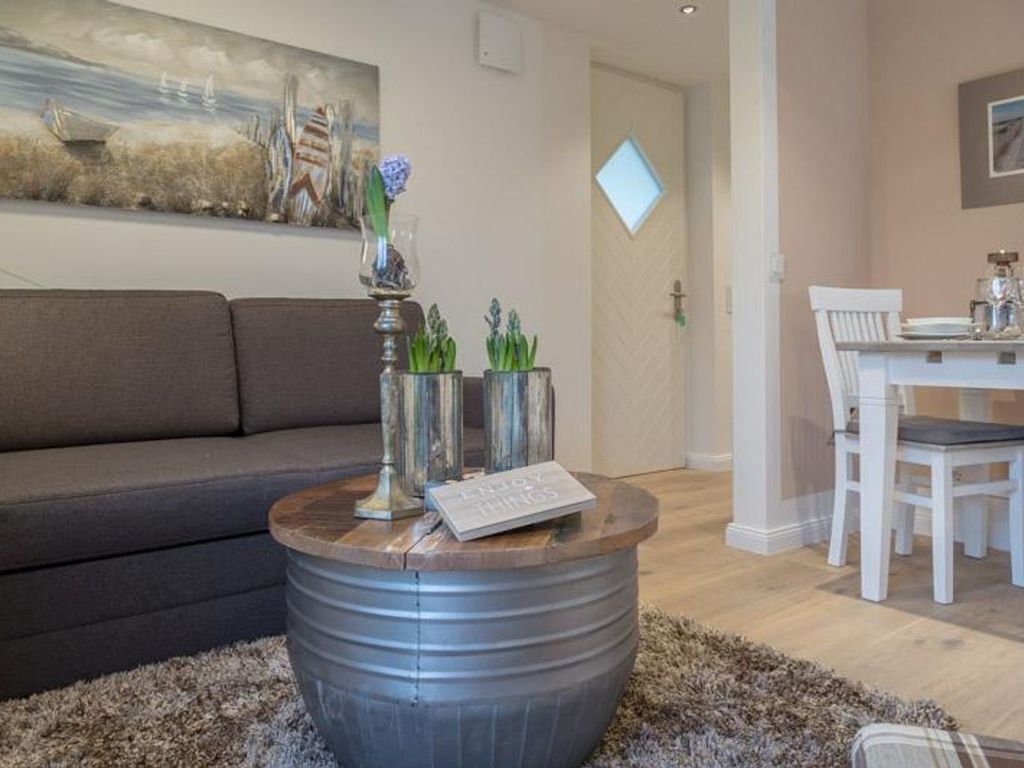 A living room with a grey sofa, a round coffee table with a book and decorative items, a dining area with a white table and chairs, and a painting on the wall.