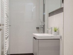 Une salle de bain moderne avec un lavabo blanc, un miroir et une plante en pot.