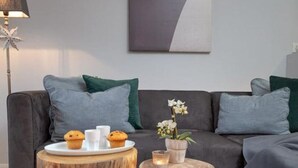 Un salon moderne avec un canapé gris, deux petites tables rondes en bois, une petite plante en pot et un élément décoratif mural.