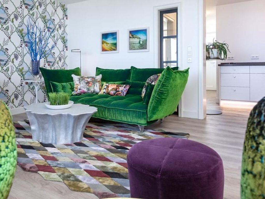 Un salon moderne avec un canapé vert, un tapis à motifs et un pouf violet.