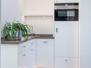 Une cuisine moderne avec des meubles blancs, un four encastré et une plante en pot posée sur le plan de travail.