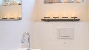 Un baño con un lavamanos blanco, un espejo y una repisa con velas.