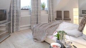 Un dormitorio moderno con cama, televisor, radiador y ventana con cortinas.