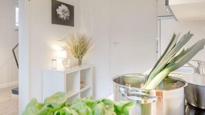 Una cocina moderna con una olla en la estufa, un estante blanco con adornos y una planta en maceta.