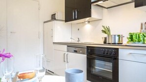 Una cocina moderna con armarios blancos, horno empotrado y una mesa de comedor con un plato de pomelo, vasos y una taza azul.