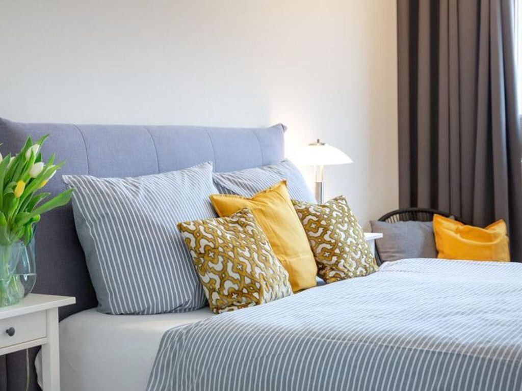 A neatly made bed with striped bedding and patterned pillows, a bedside table with a lamp, and a window with curtains.
