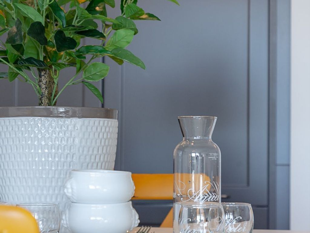 Una mesa de comedor con una planta en maceta, un florero blanco texturizado y una jarra de vidrio transparente.