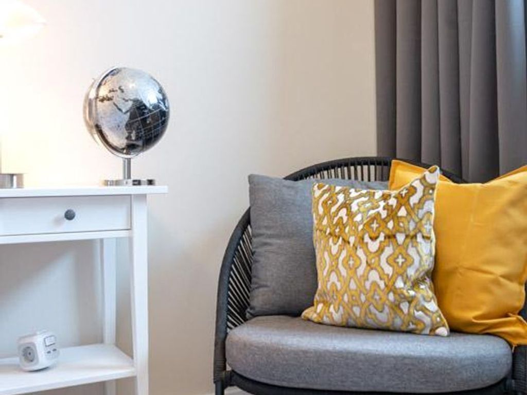 Een moderne woonkamer met een grijze bank, gekleurde kussens, een wereldbol en een witte console met een radio.