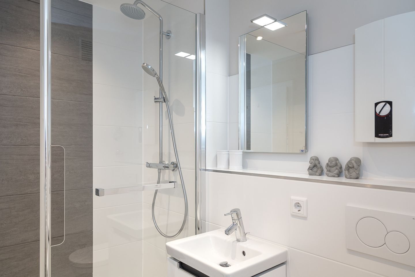 Une salle de bain moderne avec une douche à parois de verre, un lavabo blanc et un miroir au-dessus du lavabo.
