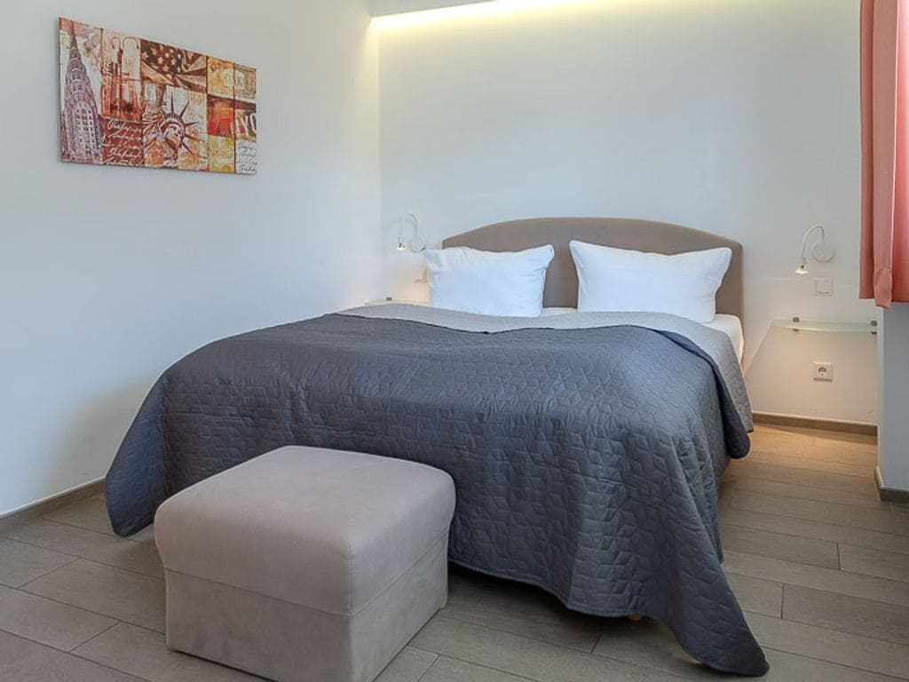 Une chambre à coucher comprenant un lit, des tables de chevet, une commode, un banc et une œuvre d’art murale.