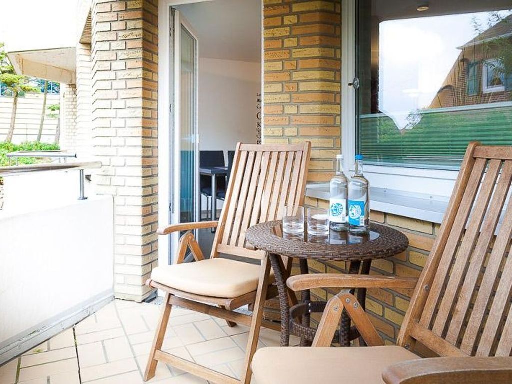 Ein Balkon mit zwei Holzstühlen, einem kleinen runden Tisch, einer Wasserflasche und einem Glas.
