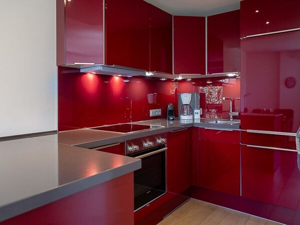 Une cuisine moderne avec des meubles de rangement rouges, des appareils électroménagers en acier inoxydable et un îlot central.
