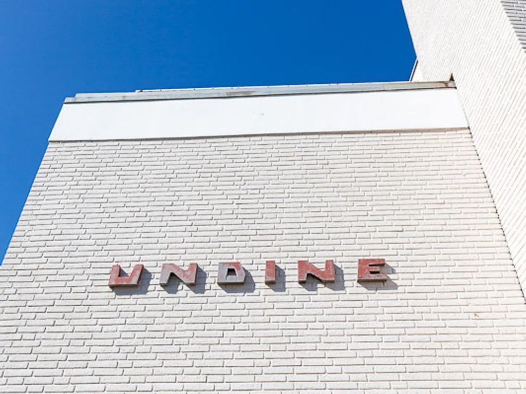 En bygnings facade med ordet "UNDINE" i røde bogstaver på en hvid murstensvæg.