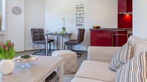 Ein modernes Wohnzimmer mit einer Couch, einem Essbereich mit Stühlen, einem kleinen Tisch mit Blumen und einer Küchenzeile mit roten Schränken.