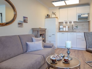Een woonkamer met een bank, een bijzettafeltje met gebakjes, en een keuken op de achtergrond.