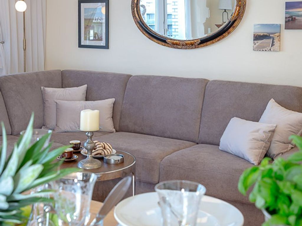 A modern living room with a grey sofa, a round mirror, and a small round table with a candle and snacks.