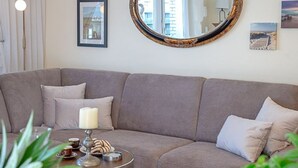 A modern living room with a grey sofa, a round mirror, and a small round table with a candle and snacks. - Black Pearl - Elisabethstraße, Dünenburg House, modern 2-room apartment with (Sylt)