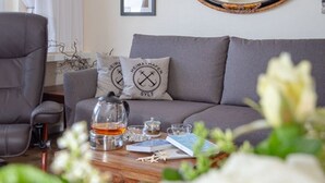 A cozy living room with a grey sofa, two matching pillows, a wooden coffee table with a teapot, cups, and books. - Black Pearl - Elisabethstraße, Dünenburg House, modern 2-room apartment with (Sylt)