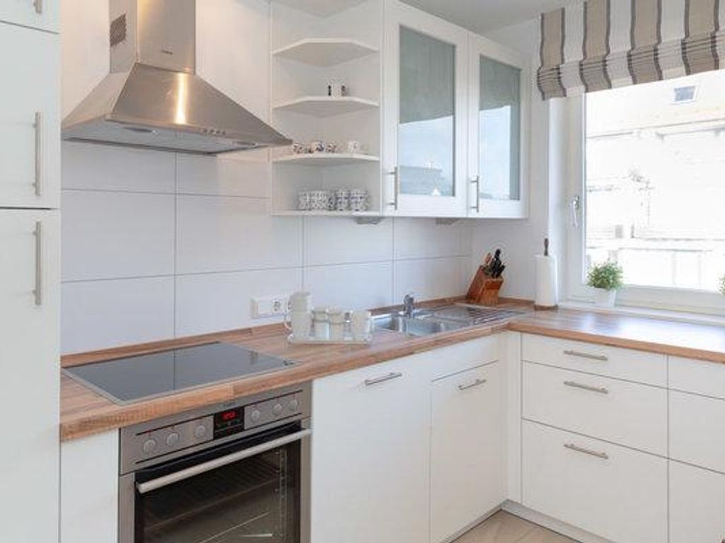 A modern kitchen with white cabinets, a stainless steel range hood, a built-in oven, and a window with a view of the outside.