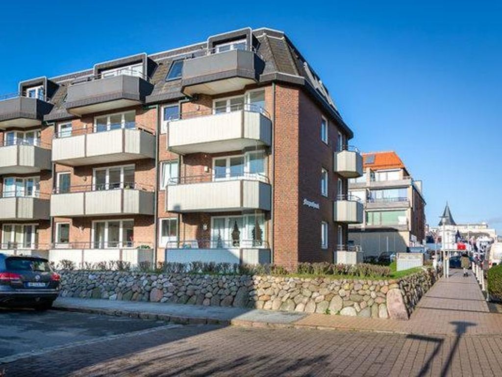 Een meerlaags woongebouw met balkons, een stenen muur ervoor en een heldere lucht.