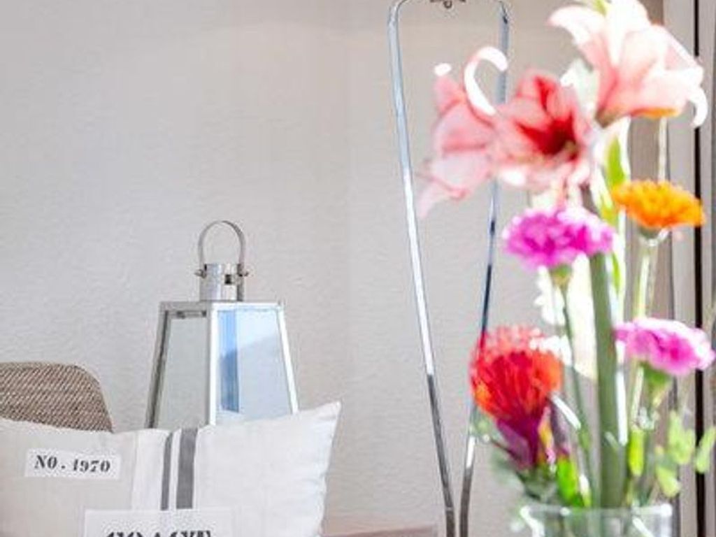 Une chambre avec un lit, une table de chevet, une lampe et un vase de fleurs.