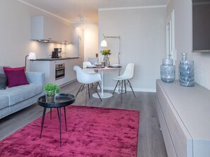 A modern living room with a grey sofa, a red rug, and a dining area with white chairs and a table.
