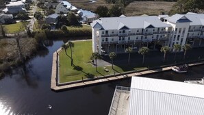 Un hotel frente al agua con varios balcones, un área verde con palmeras y un muelle.