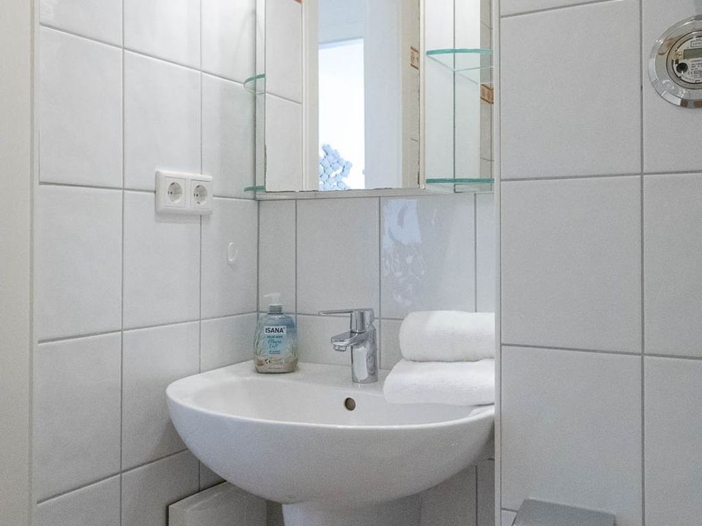 Un baño con un lavamanos blanco, un espejo y una repisa de vidrio.