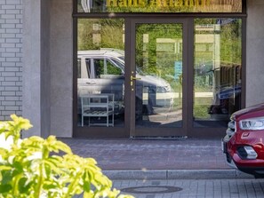 Un bĂątiment avec une entrĂ©e dotĂ©e dâune porte en verre, une voiture visible garĂ©e Ă lâextĂ©rieur et une voiture rouge garĂ©e devant.