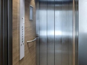An elevator with a metallic interior, a control panel with buttons, and a wooden wall.