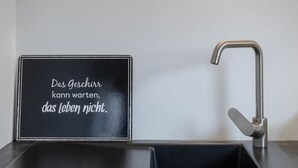Une cuisine avec un tableau noir où est affichée une citation allemande, un robinet moderne et un plan de travail.
