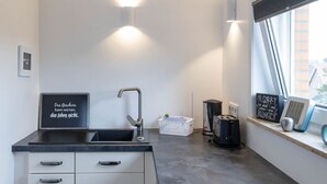 Une cuisine moderne équipée d’une cuisinière intégrée, d’un évier et d’une fenêtre avec des stores.
