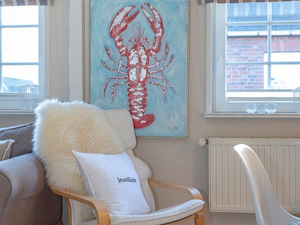 A cozy room with a wooden chair, a fluffy pillow, and a painting of a lobster on the wall.