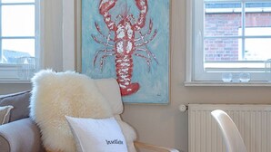 A cozy room with a wooden chair, a fluffy pillow, and a painting of a lobster on the wall. - House Senwai - Surfside 2 - Top modern 3 room apartment SURFSIDE 1 in quiet, (Sylt)