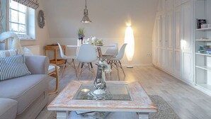 A modern living room with a sofa, a coffee table, and a dining area with chairs and a table. - House Senwai - Surfside 2 - Top modern 3 room apartment SURFSIDE 1 in quiet, (Sylt)