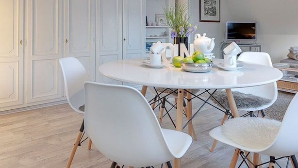 A dining area with a round table, white chairs, and a chandelier. There is a bookshelf in the background and a television on a stand. - House Senwai - Surfside 2 - Top modern 3 room apartment SURFSIDE 1 in quiet, (Sylt)