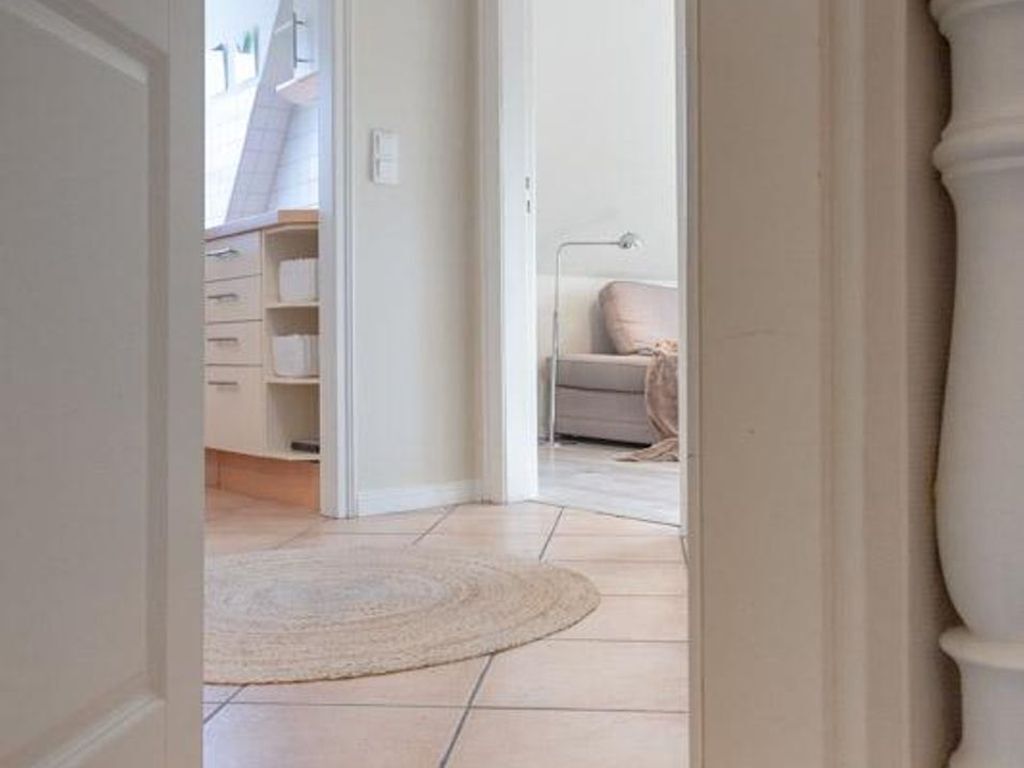 A hallway leading to a bedroom with a bed, a bedside lamp, and a white door.