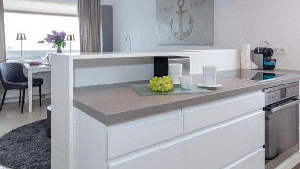 Una cocina moderna con una isla central, un comedor con mesa y sillas, y vista al mar.