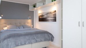 Un dormitorio moderno con una cama grande, cabecera, estante con plantas y un cuadro enmarcado.