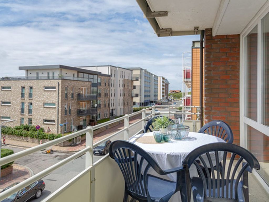 A balcony with a table and chairs, overlooking a street with buildings and a clear sky.